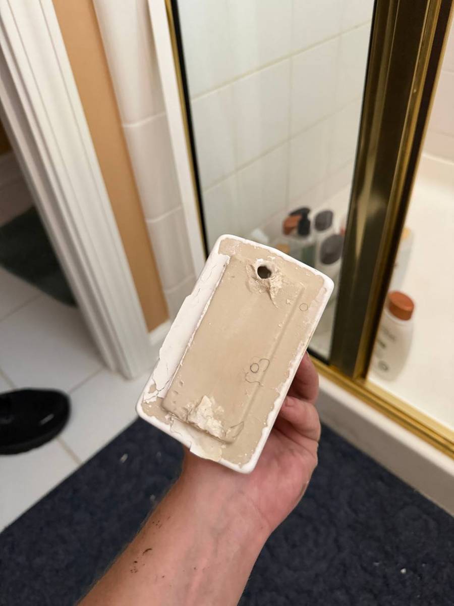 Old adhesive being cleaned off the back of the ceramic towel holder before re-mounting