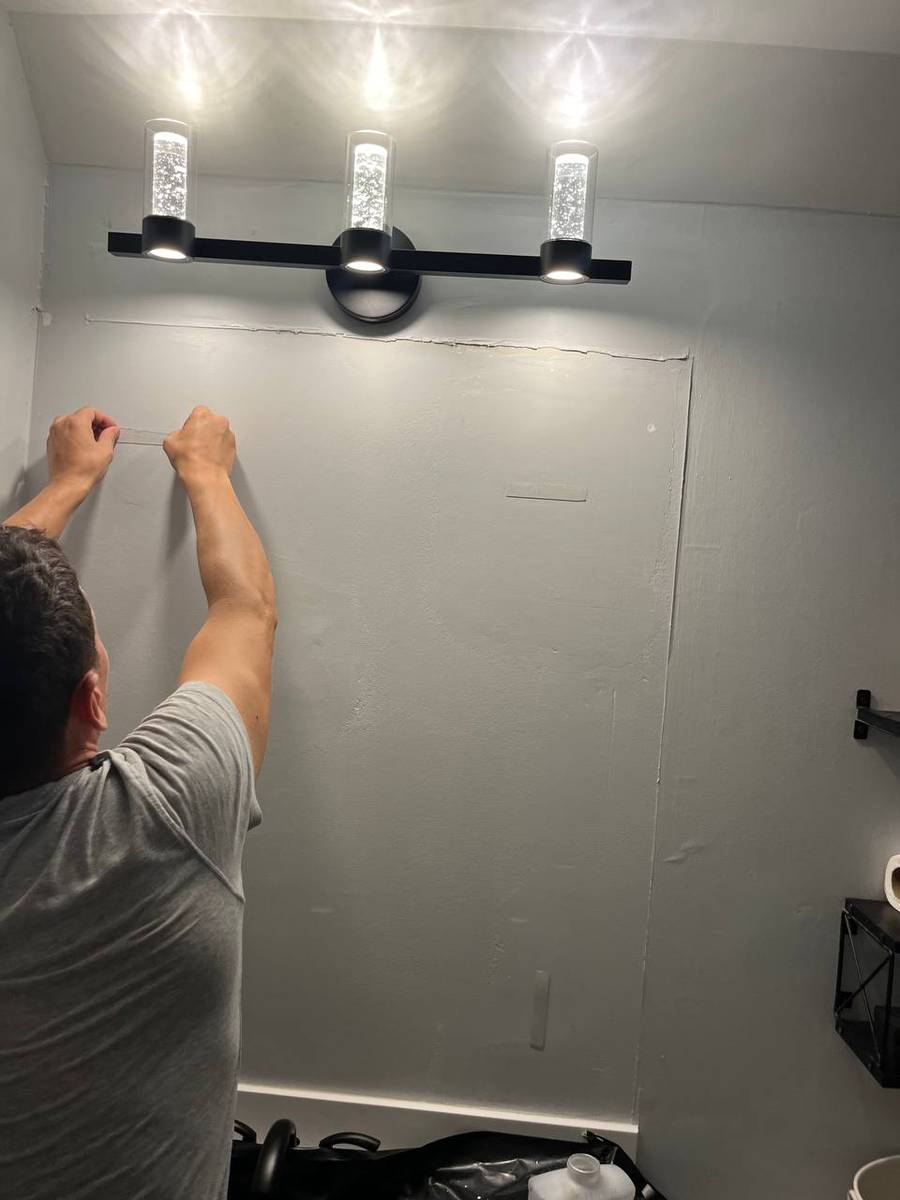 Applying mirror-safe adhesive to the wall above a bathroom vanity before mounting a frameless mirror