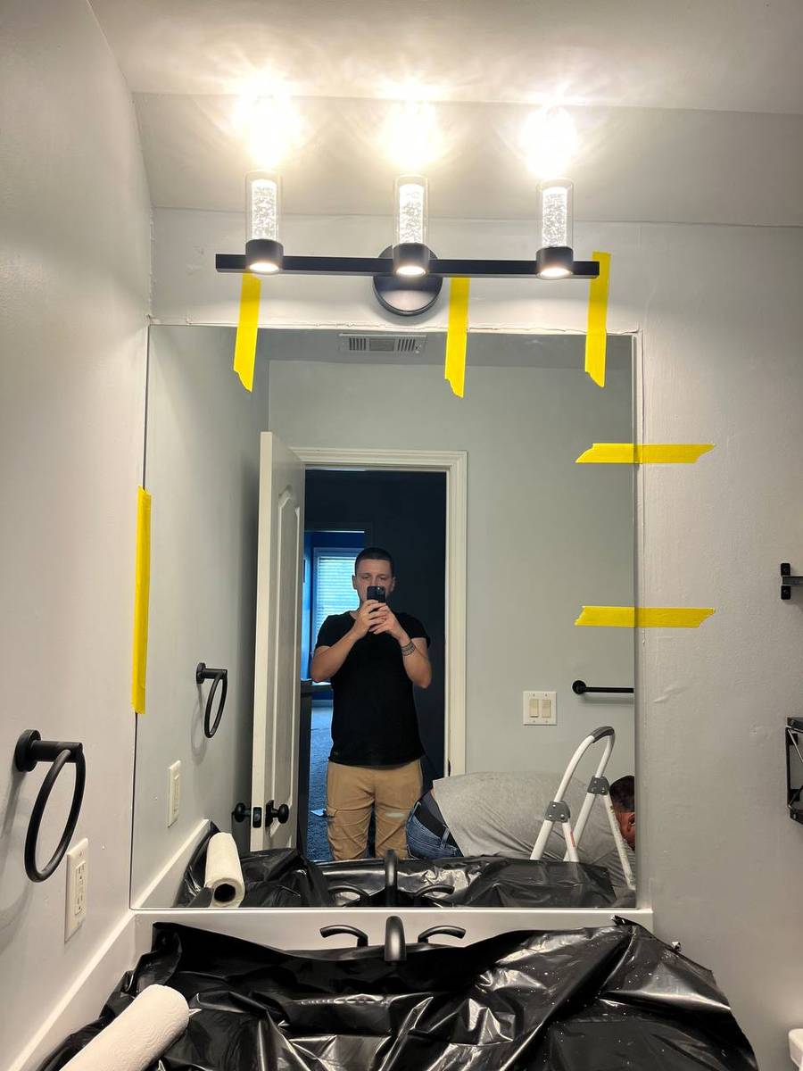 Frameless bathroom mirror mounted above the vanity, taped in place while the adhesive cures